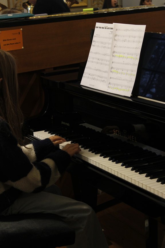 Eine Jugendliche von schräg hinten an einem Klavier.