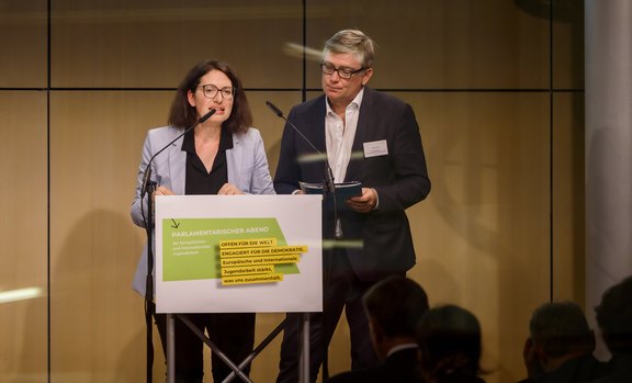 Eine Frau und ein Mann stehen auf einer Bühne an einem Podium und halten eine Rede.