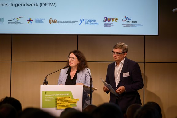Zwei Personen stehen auf einer Bühne und halten eine offizielle Rede