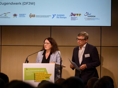 Zwei Personen stehen auf einer Bühne und halten eine offizielle Rede