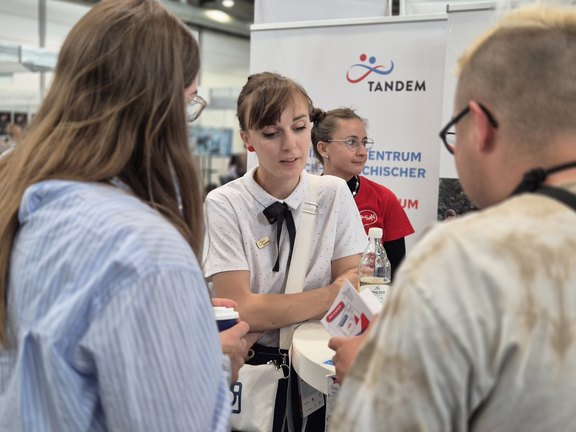Frau spricht mit Personen an einem Messestand