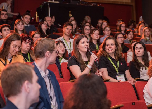 Junge Menschen verfolgen in einem Kinosaal ein Bühnenprogramm.