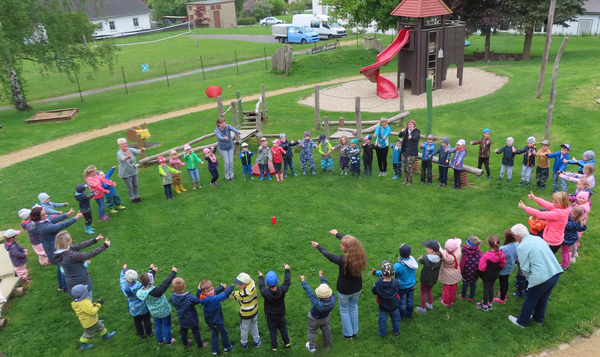 Kindergartenkinder stehen in einem großen Kreis auf einer Wiese