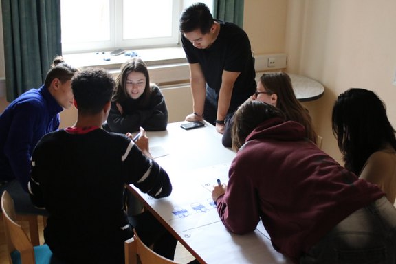 Junge Menschen sitzen um einen Tisch und diskutieren über ein Thema.